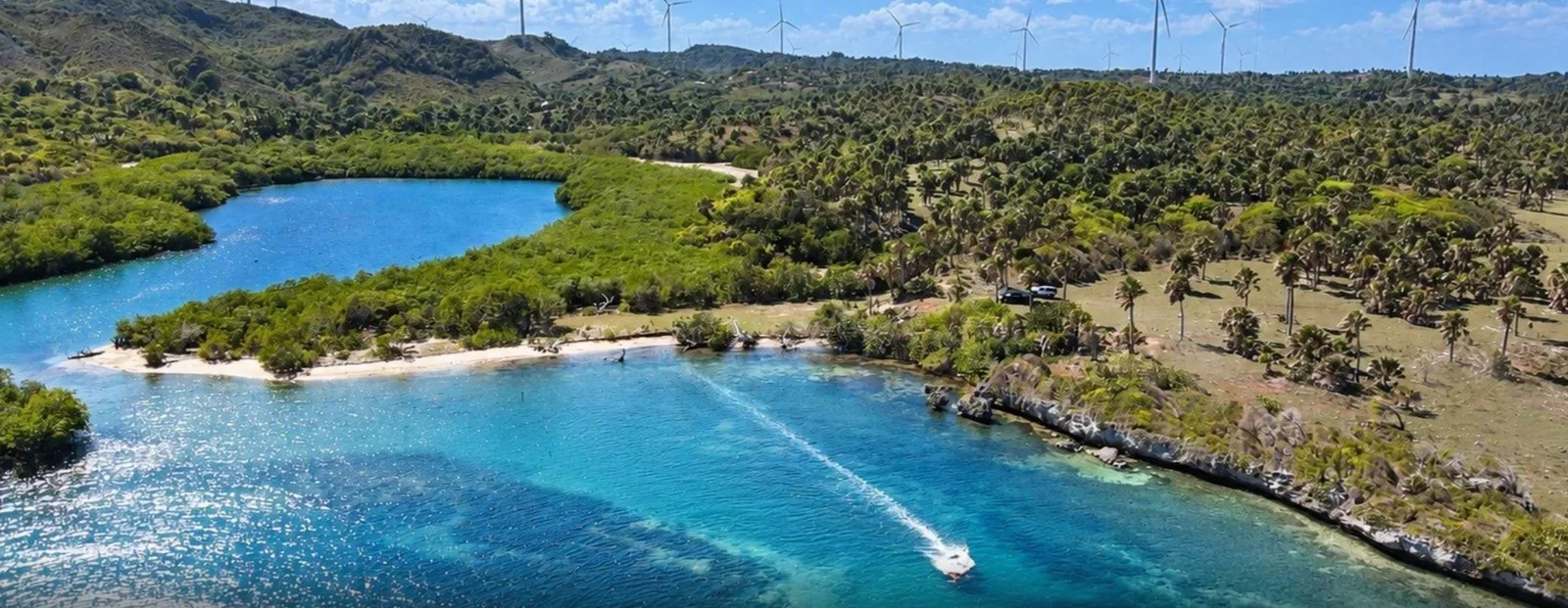 La entrada de la bahía con una embarcación; detrás, la laguna y aerogeneradores en la cresta