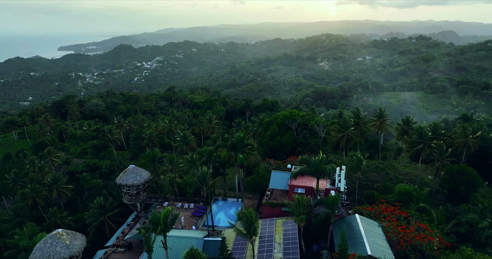 Telhados com painéis solares e uma torre de palha, com a costa ao longe