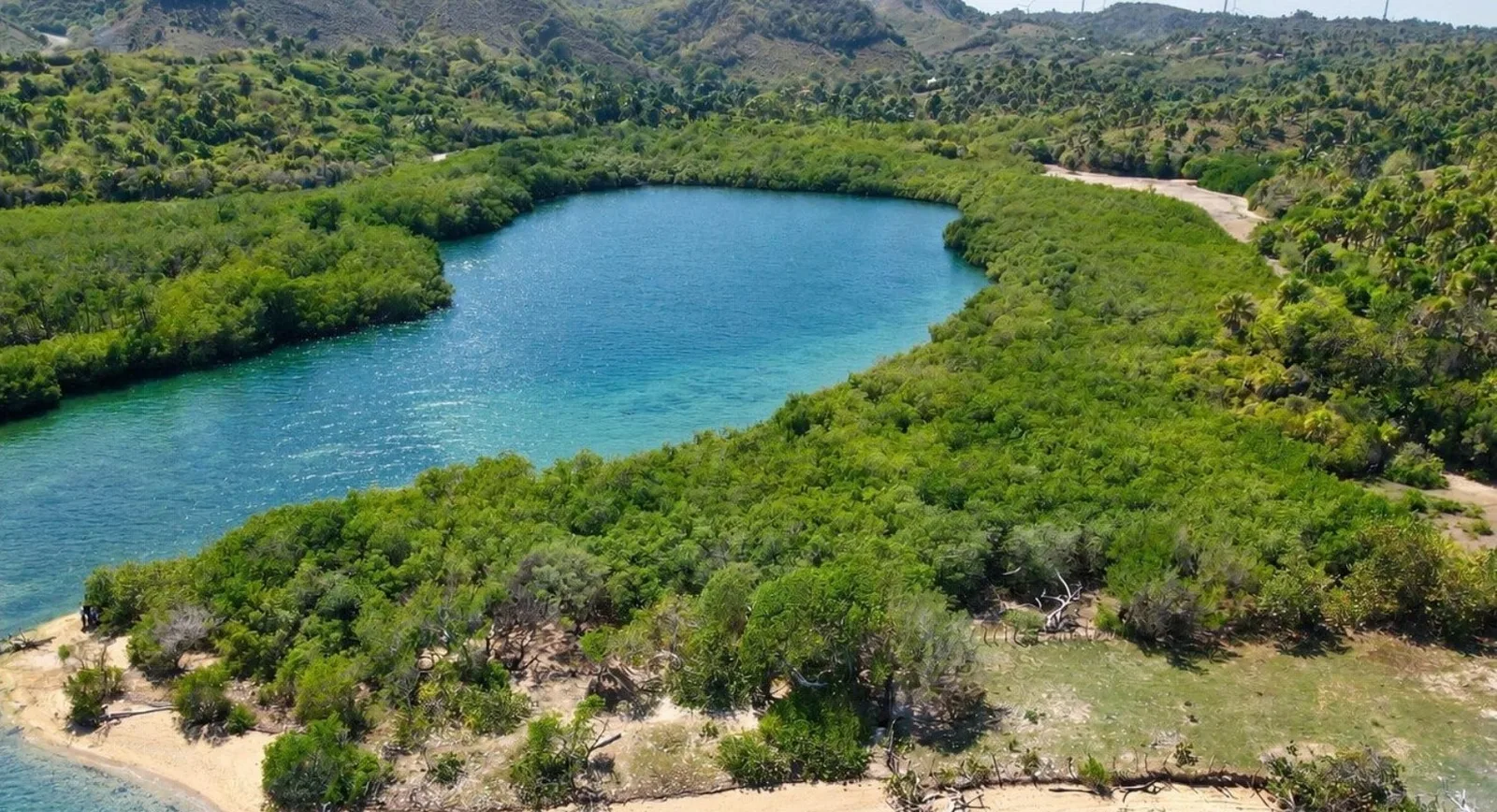 Laguna interior rodeada de manglares y colinas verdes, con una orilla de arena delante
