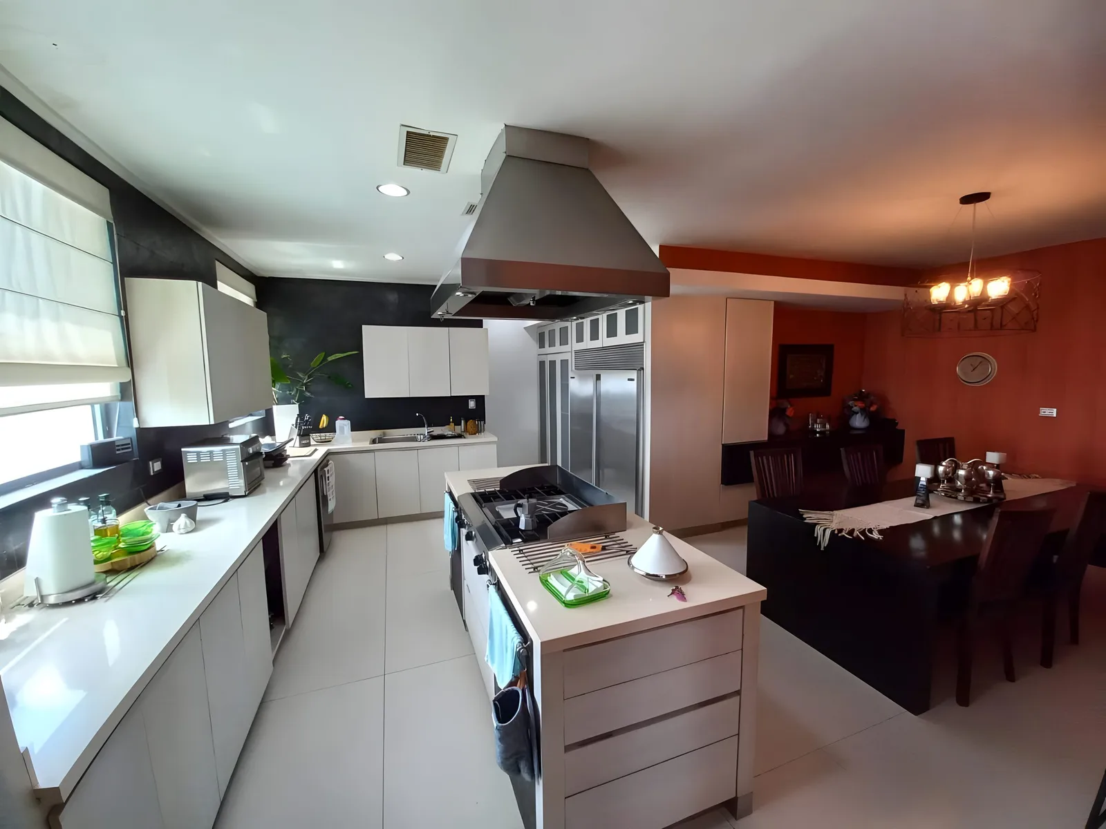 Kitchen with a centre island, steel hood and a dining table beyond
