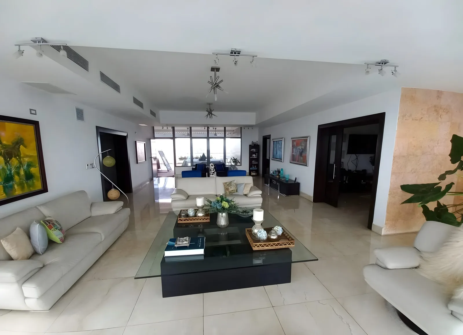 Long living room with cream sofas, a glass coffee table and windows at the far end
