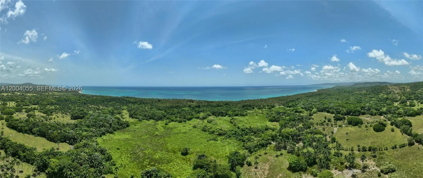 Amplia panorámica de pastos y lomas arboladas, con el mar a lo lejos