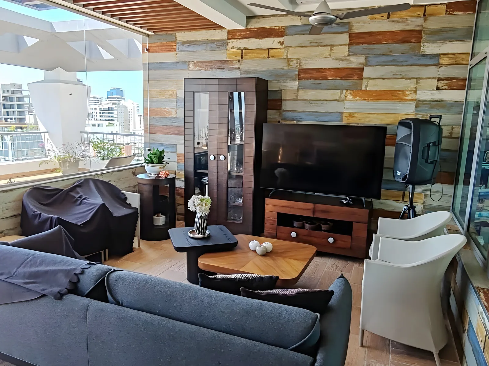Covered terrace lounge with a plank-clad wall, a television, a loudspeaker and sofas