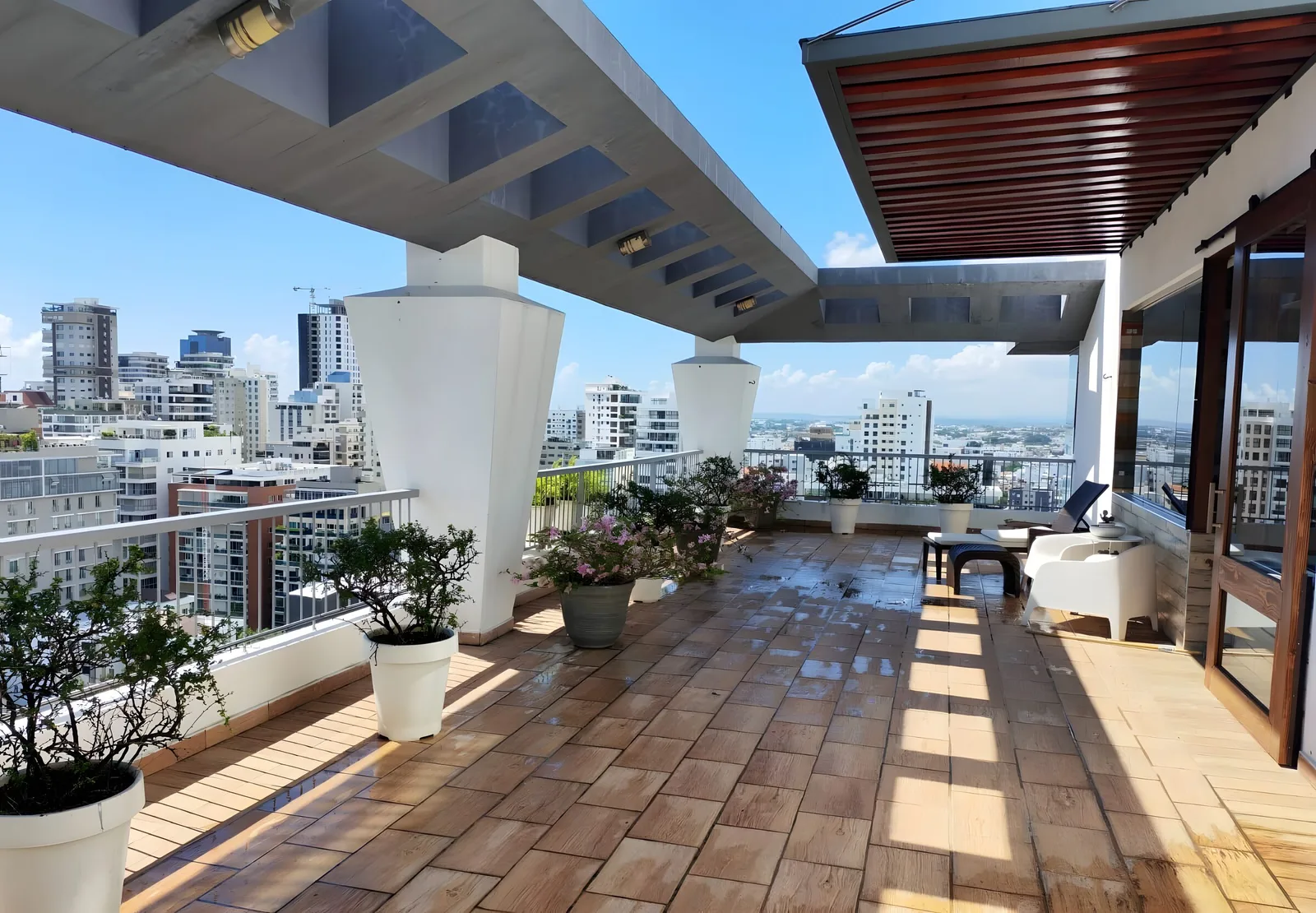 Tiled roof terrace with a pergola and potted plants, city towers beyond the railing